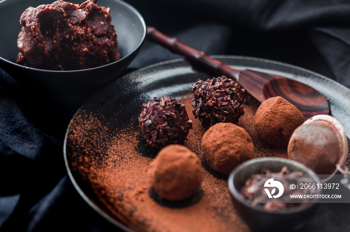 Date energy ball with cocoa on a black dish and cocoa nibs