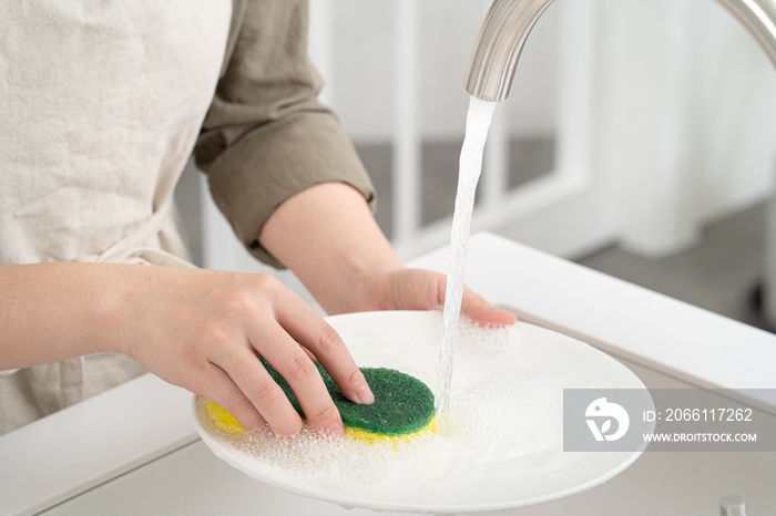 Woman housekeeper is doing the dishes at home kitchen.