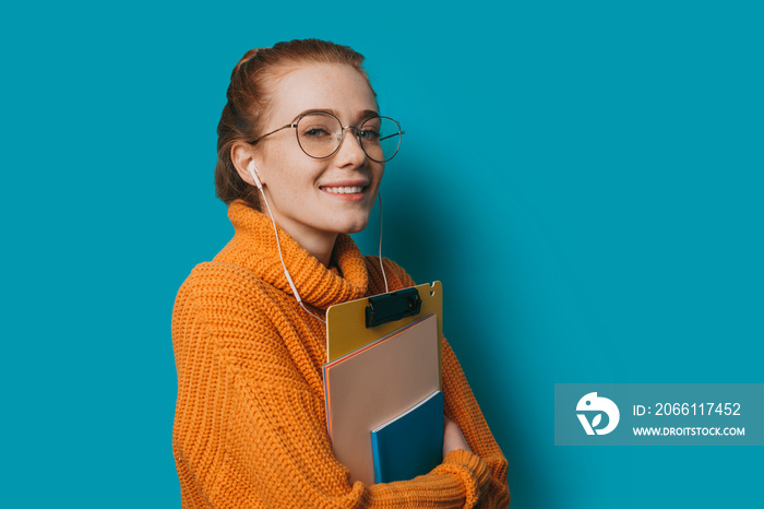 Portrait of a young charming female student with red hair and freckles wearing glasses looking at ca