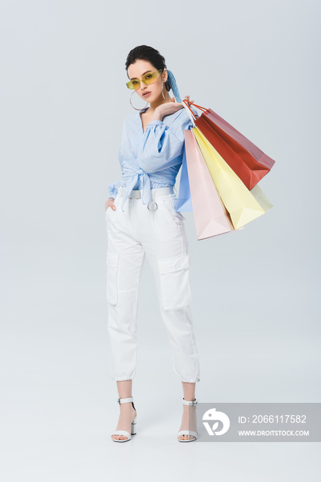 beautiful fashionable girl holding shopping bags and looking at camera on grey