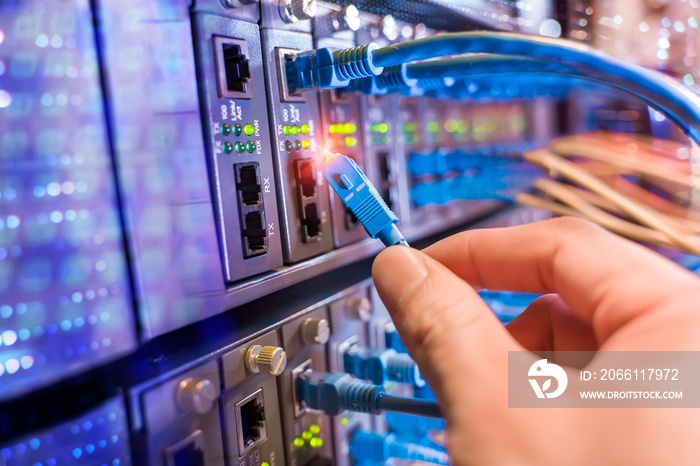 man working in network server room with fiber optic hub for digital communications and internet