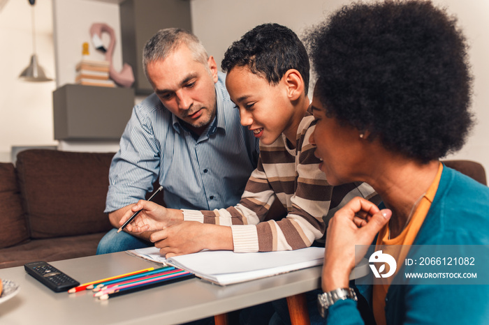 Parents helping their son with his homework at home in living room.