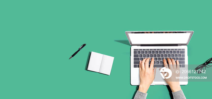 Person using a laptop computer with a notebook and eyeglasses - Flat lay