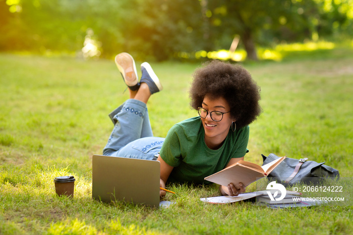 黑人少女躺在公园的草地上，学习，使用笔记本电脑