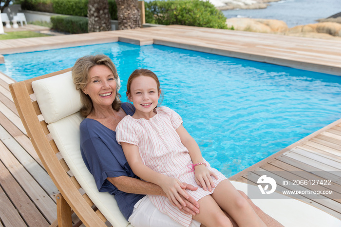 Portrait happy grandmother and granddaughter relaxing at poolside