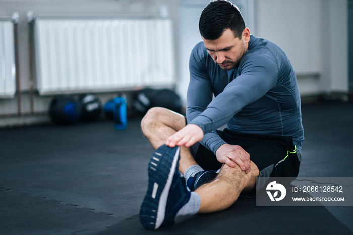 Muscular man stretching his legs before workout.