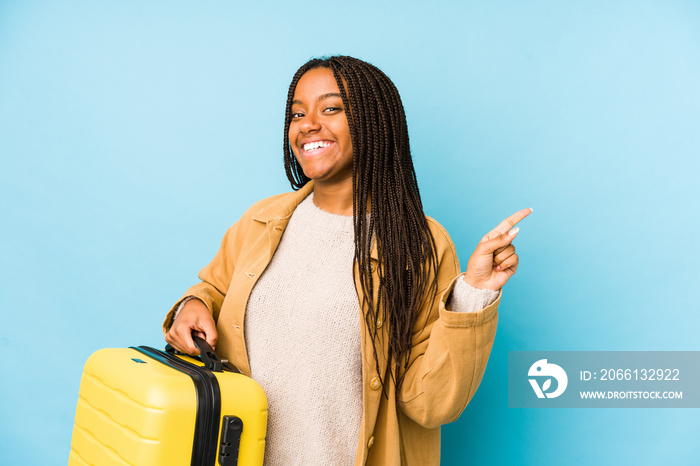 Young african american traveler woman holding a suitcase isolated smiling and pointing aside, showin