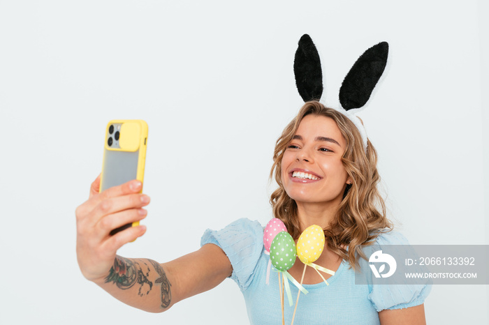 Happy Easter greetings, young woman wearing bunny ears holding colored eggs