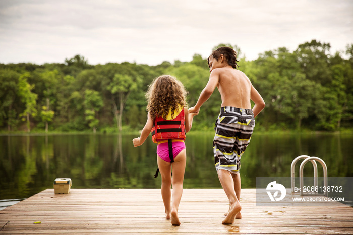 Rear view of siblings jumping into lake