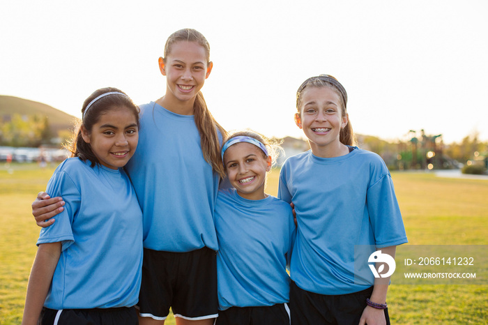 Portrait of smiling girls standing on soccer field against clear sky during sunset