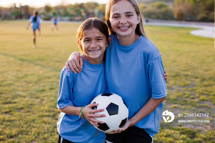 Portrait of smiling friends holding soccer ball in grassy field