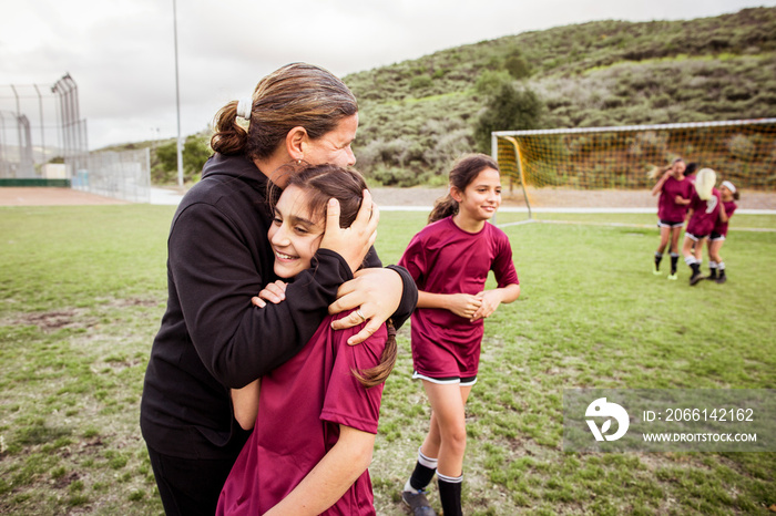 Coach embracing smiling girl on soccer field