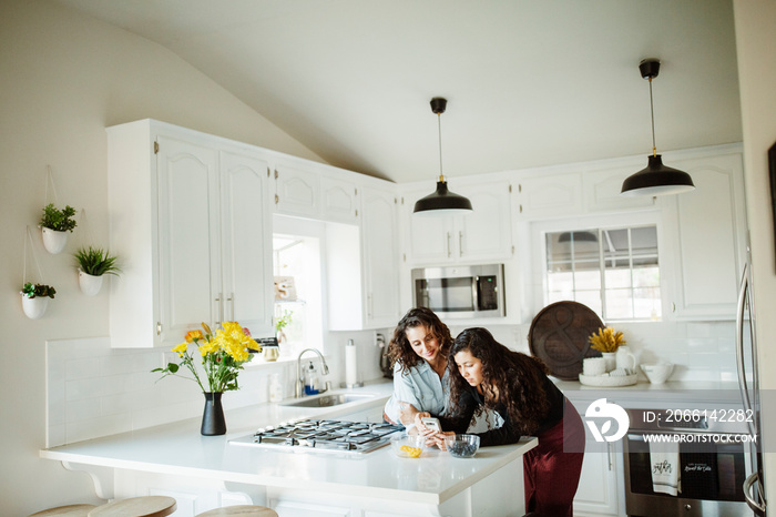 Mother with daughter using smart phone on kitchen counter at home