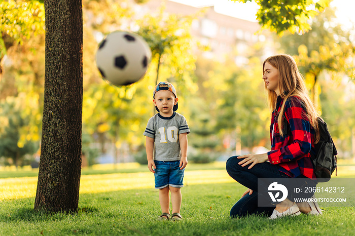 年轻快乐的妈妈和小儿子在公园里踢足球