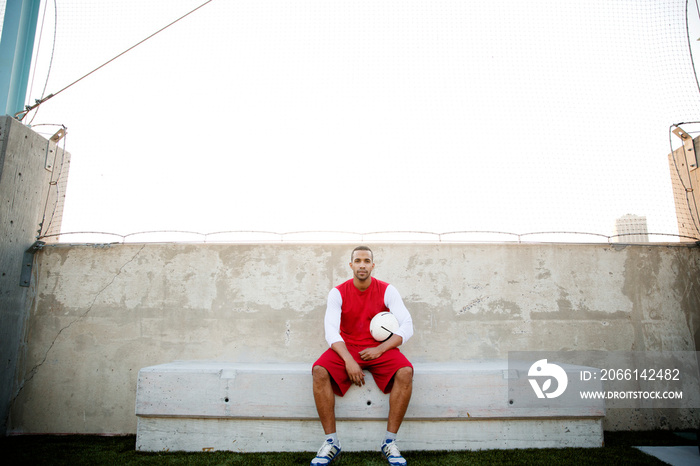 Portrait of athlete with soccer ball sitting on bench