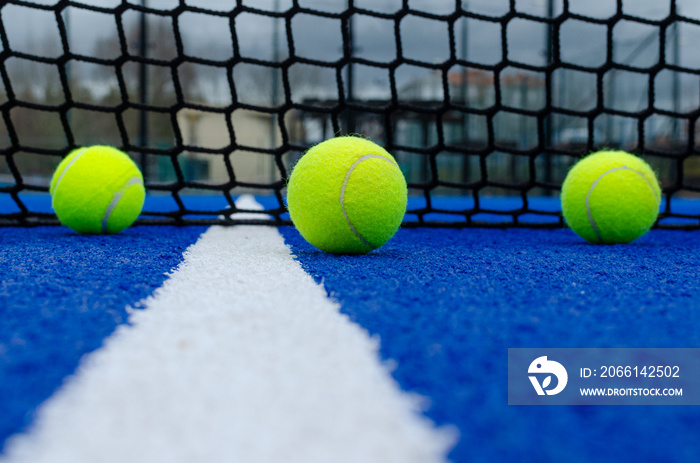 Selective focus. Net of a blue paddle tennis court and three balls near the white line
