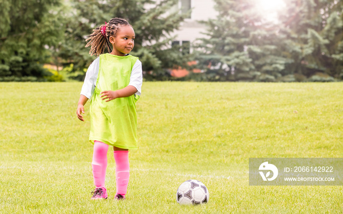 一个年轻的非裔美国女孩正在学习如何在阳光明媚的日子踢足球