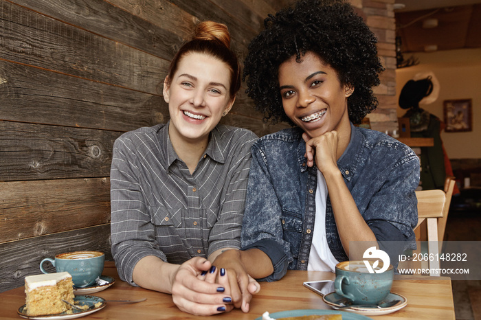 Two lesbians of different races having nice time together at coffee shop, drinking fresh cappuccino 