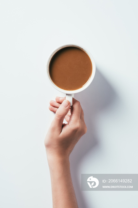 cropped shot of woman holding cup of coffee on white surface