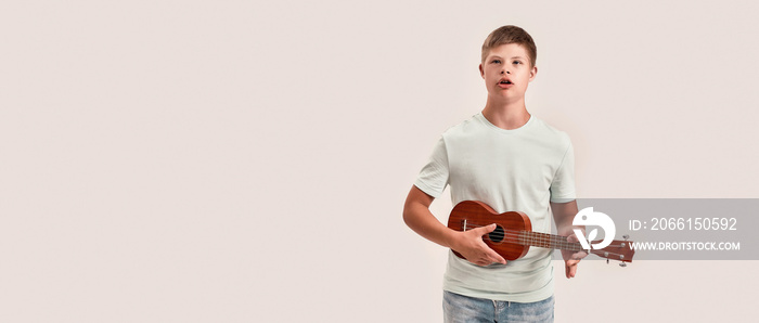 Teenaged disabled boy with Down syndrome holding, playing ukulele guitar, standing isolated over whi