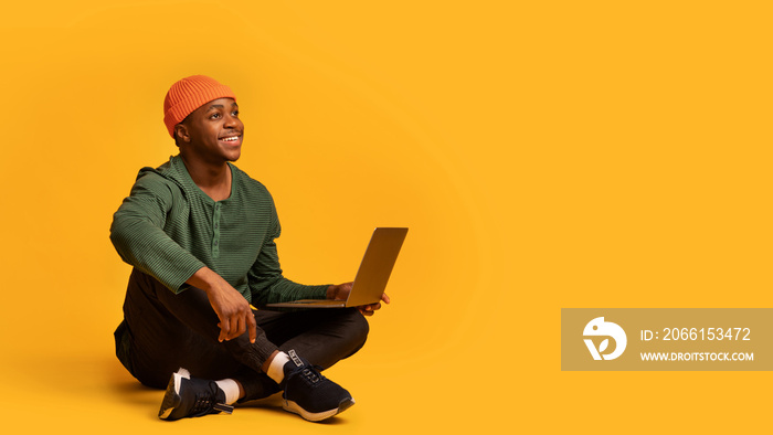 Online Offer. Smiling young black guy sitting with laptop and looking away