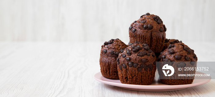 Chocolate cupcakes on a pink plate over white wooden background, side view. Copy space.