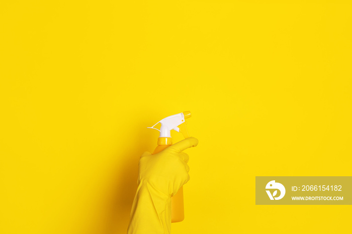 hand in a glove with a spray bottle over yellow background, cleaning concept