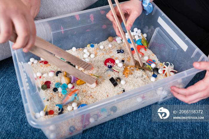 Pediatric Sensory integration therapy - two kids picking up small objects with tongs from a rice con