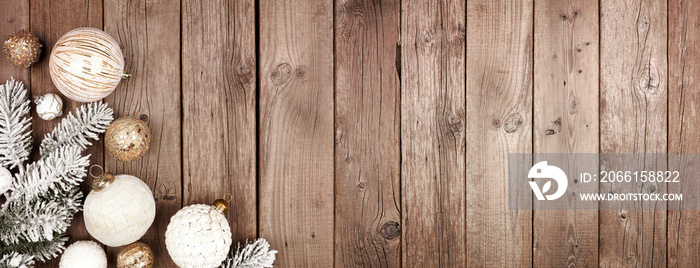 Christmas corner border of white and gold ornaments with snowy branches. Top view on a rustic wood b