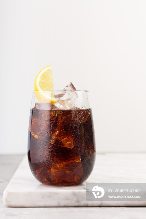 Glass of cola with ice and lemon on the white background, vertical