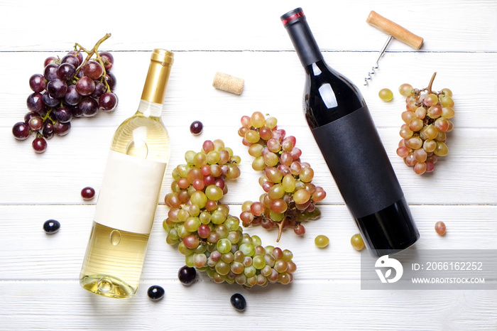 带有空白哑光标签的红葡萄酒和白葡萄酒年份瓶，开瓶器和葡萄，木质餐桌背景