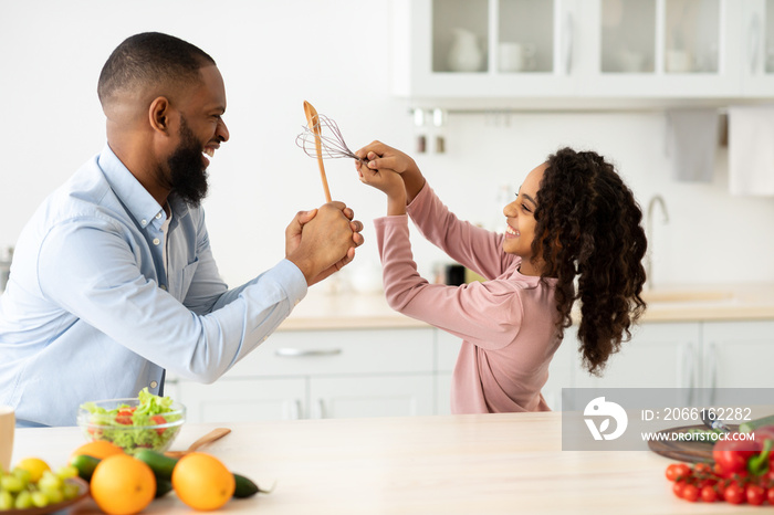 Black father and daughter having silly fight in the kitchen