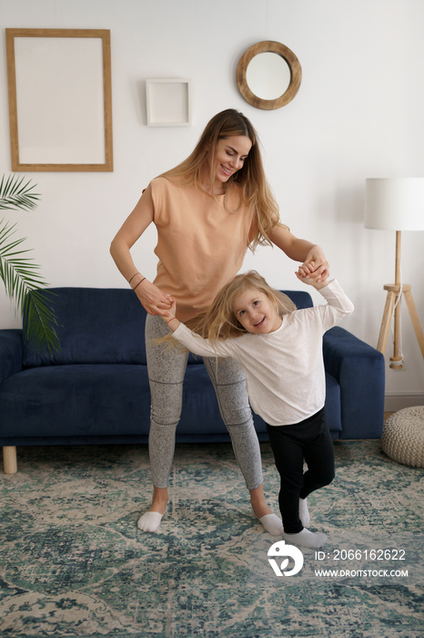 Carefree funny caucasian family young mom having fun with cute little kid girl jump dancing in livin