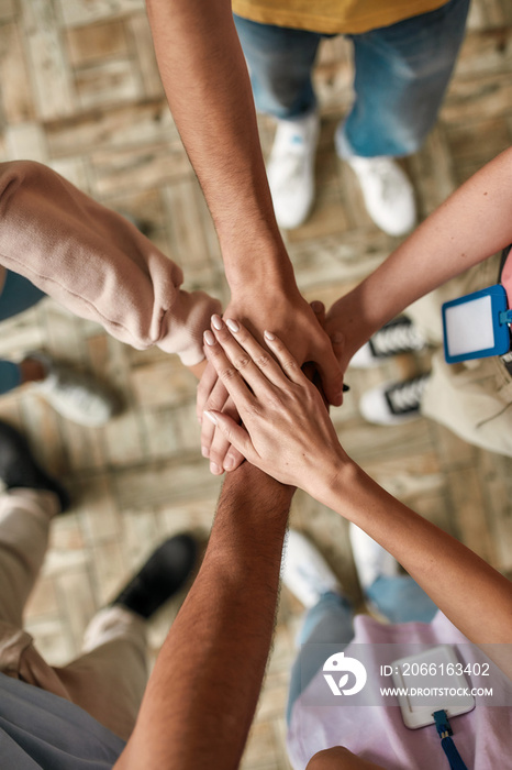 Top view of diverse young volunteers putting their hands on top of each other like a real team while