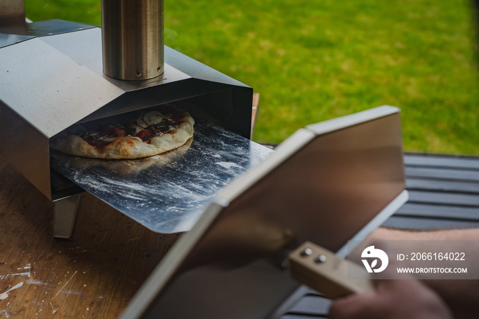 Man is pulling a delicious fresh home made pizza out of a stainless steel home portble oven fueled b