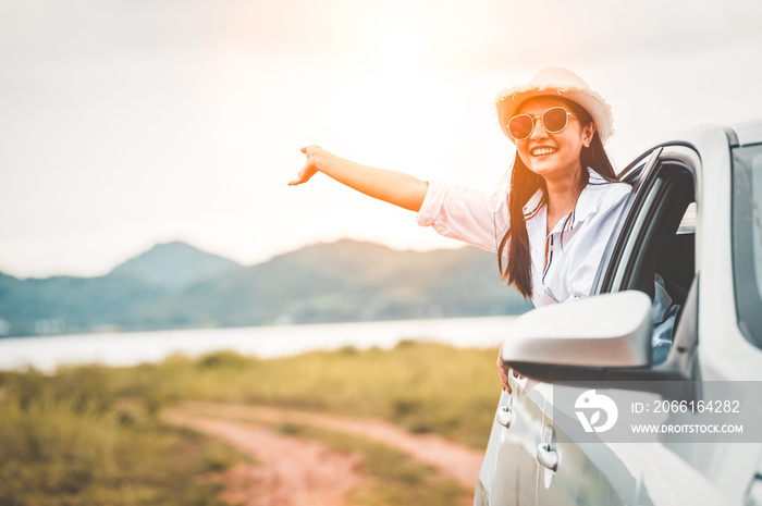 Happy woman waving hand outside open window car with meadow and mountain lake background. People lif