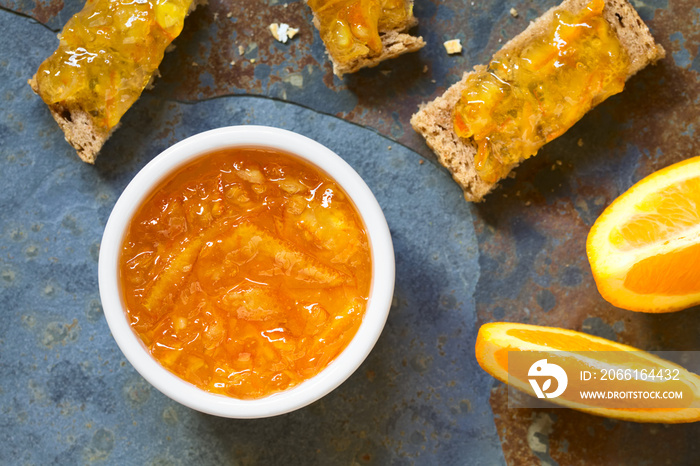 Orange jam in small bowl with bread and orange wedges on the side, photographed overhead on slate wi