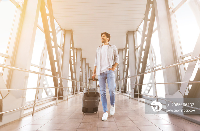 Young millennial guy walking with suitcase at airport