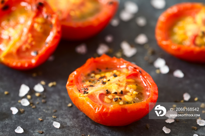 Roasted cherry tomato halves with salt and pepper, photographed closeup on slate with natural light 