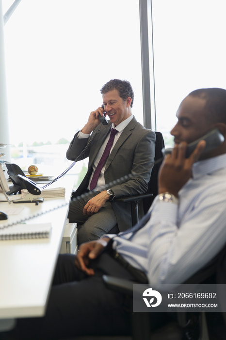 Businessmen talking on telephones in office