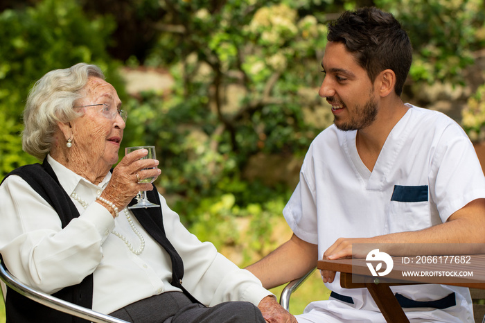 Senior woman sitting in garden next to male assistant.