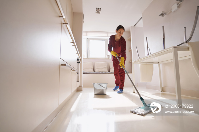 Concentrated uniformed professional janitor doing wet cleaning