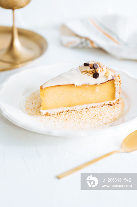 French flan on white plate with biscuit crumbs around, with almonds on top. Piece of cake on white b