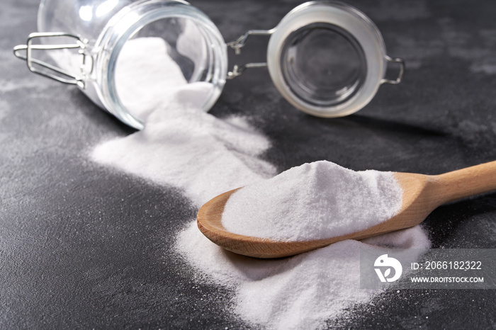 Baking soda  in a wooden spoon on a black background .