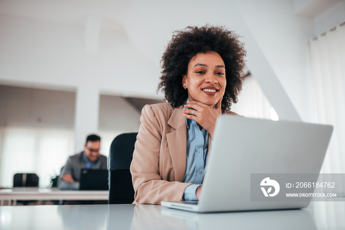 Cheerful brunette lady in bright office working on laptop.