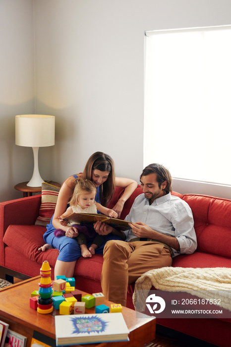 Parents reading book to little daughter in living room