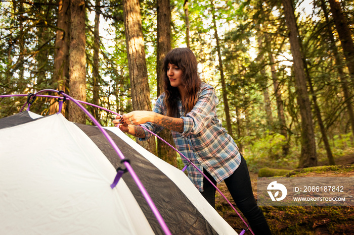 Young woman setting up tent in forest