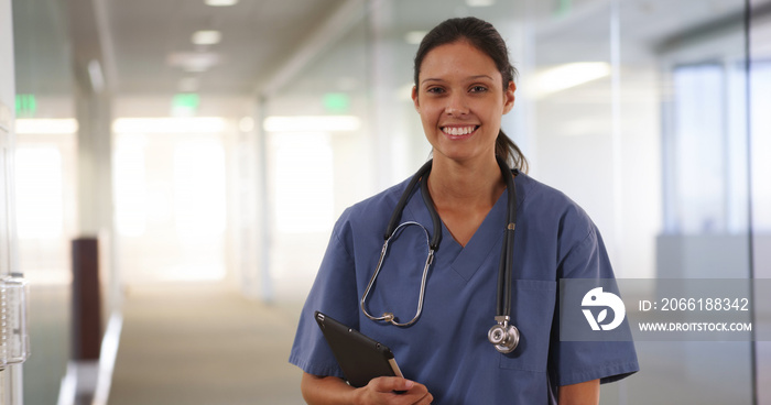 Happy millennial woman nurse or doctor smiling at camera in hospital hallway