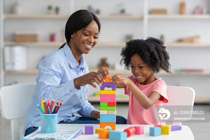 Adorable black kid and child development specialist playing with bricks