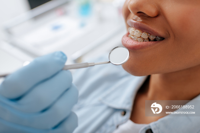 cropped view of orthodontist in latex glove holding dental mirror near happy african american patien